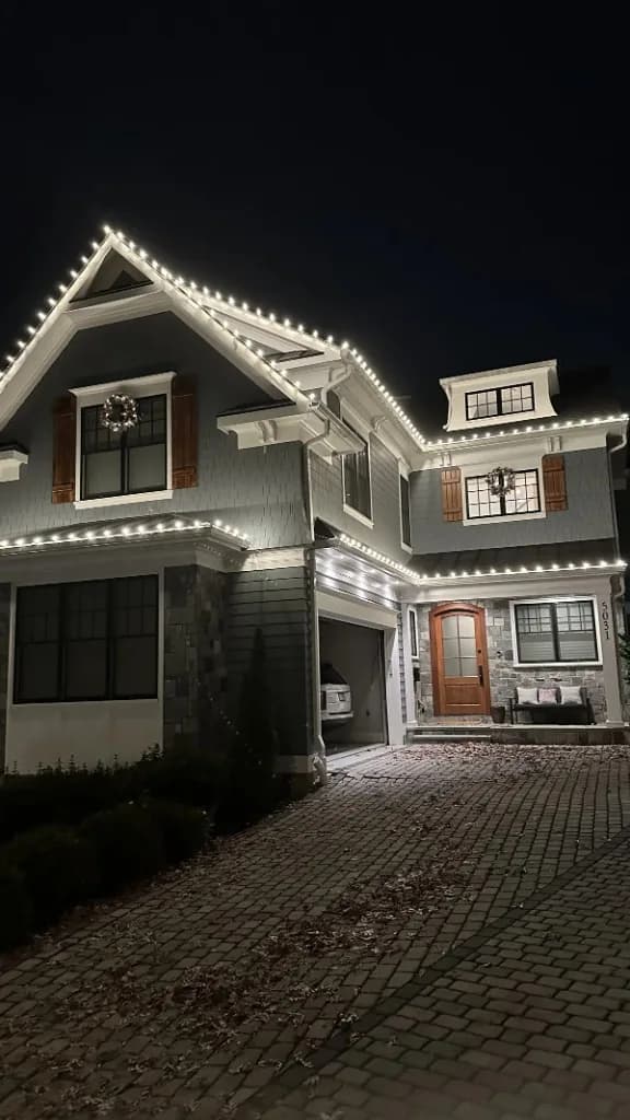 Christmas light installation in the DMV — warm white roofline and wreath accents at night