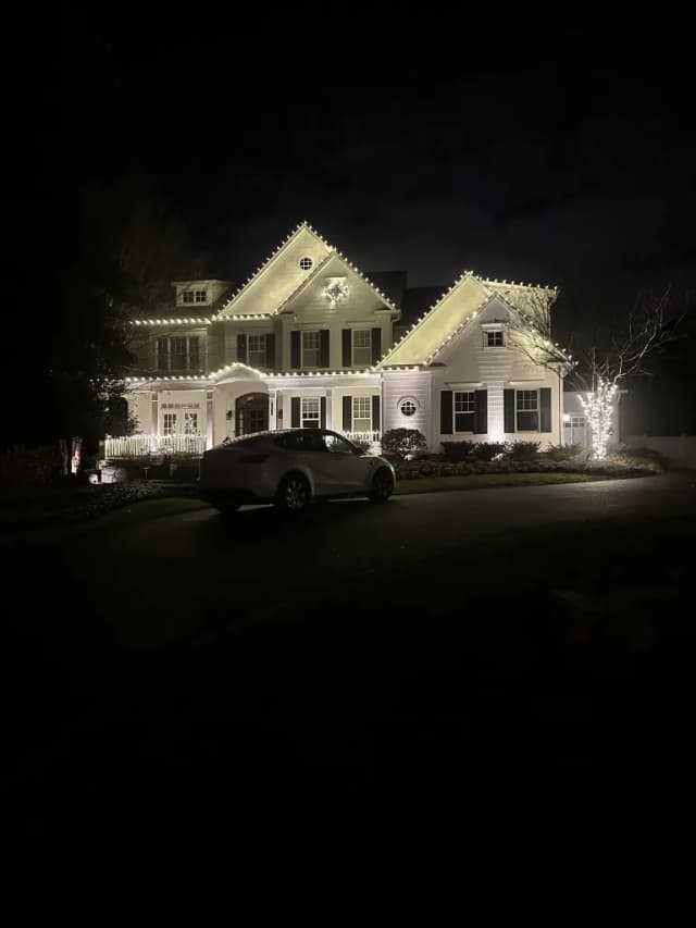 Christmas light installation in the DMV — warm white roofline and wreath on a stone-front home