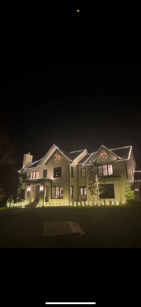 Luxury white home at night with warm white roofline holiday lights and wreaths