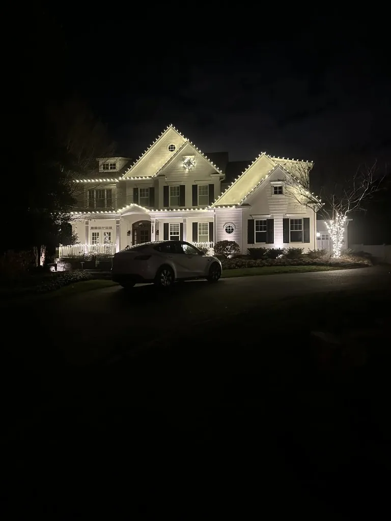Christmas light installation in the DMV — warm white roofline and wreath on a stone-front home